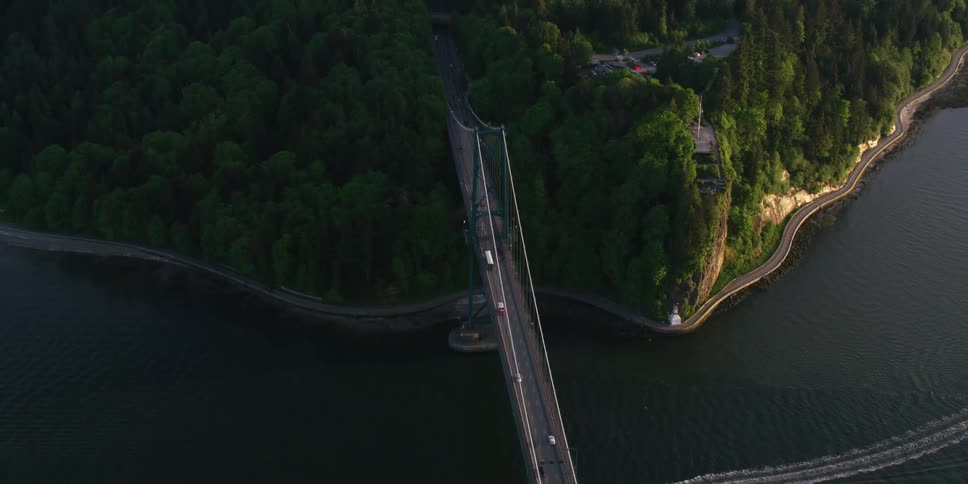 An aerial view of vehicles driving across a bridge as a boat sails beneath