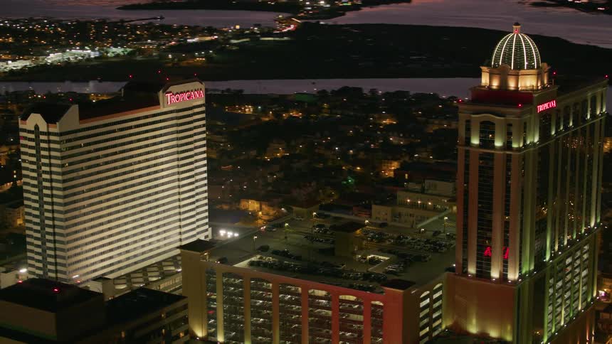 Two tropicana buildings sit in brightly lit city near water with parking garage between them