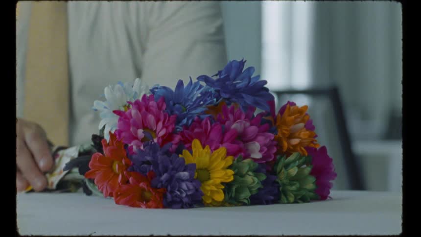 Man sits at table and reaches out to touch a colorful bouquet of flowers