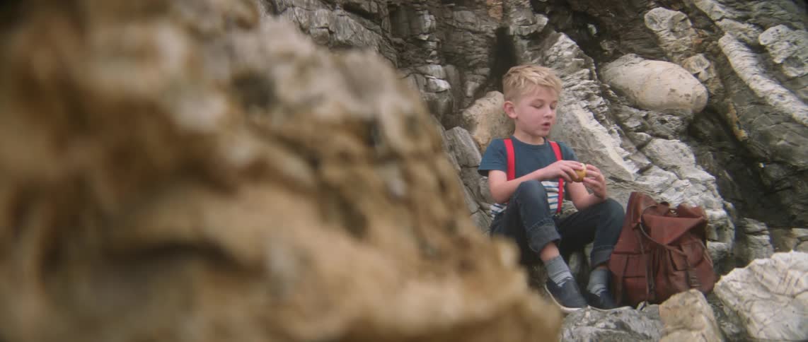 A boy is sitting near rocks eating
