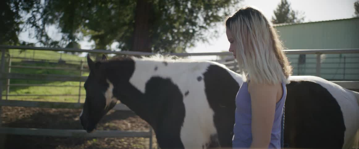 A blonde woman walking alongside a horse in a corral at at ranch