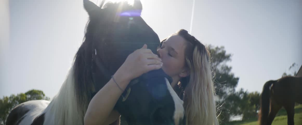A horse moves its head as a woman hugs kisses and pets it