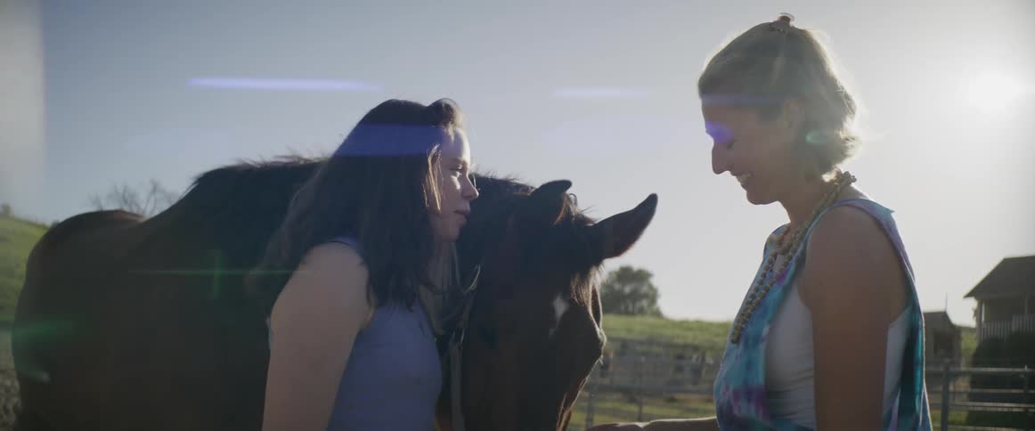 A young woman talks with an older woman as they stand near a horse in a corral during the day