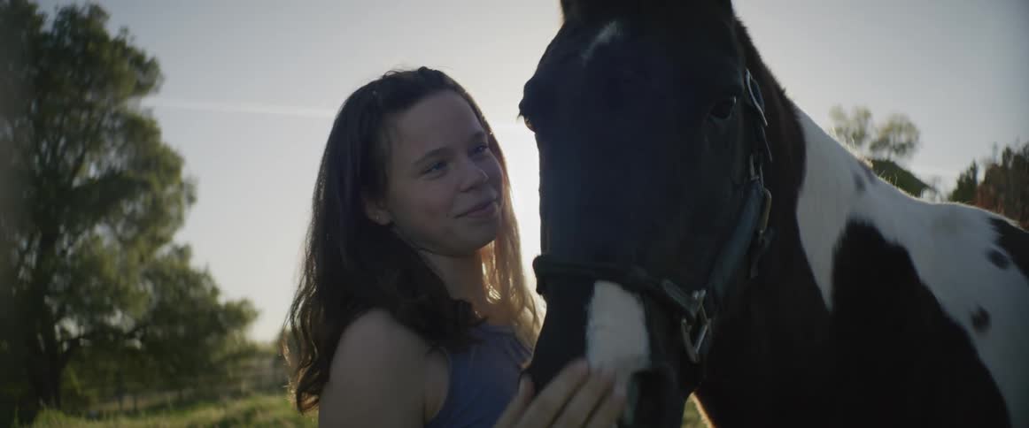 A teenager smiles while petting her horse