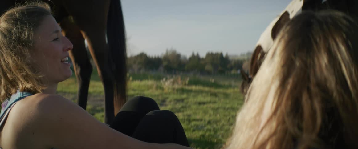 Two women are talking outdoors next to horses at a farm