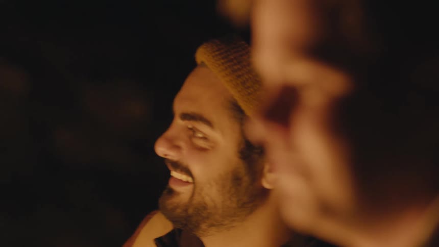 Two men sit outside by a fire and laugh