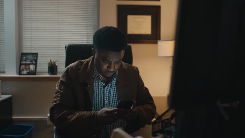 Nervous man working at the office picks up his phone and starts texting frantically