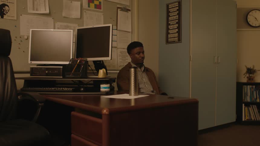 A man sitting alone in an office leans forward to put his face in his hands