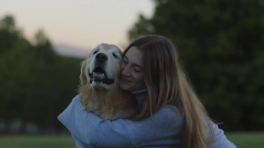 Woman hugs and kisses dog as they sit in park