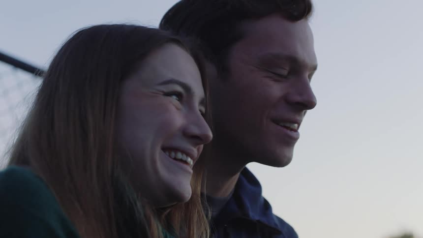 A young man and woman laugh together and she leans her head on his shoulder