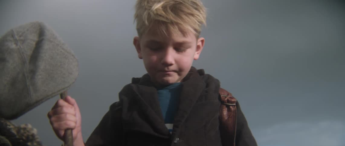 A boy with a hat on a stick looks down