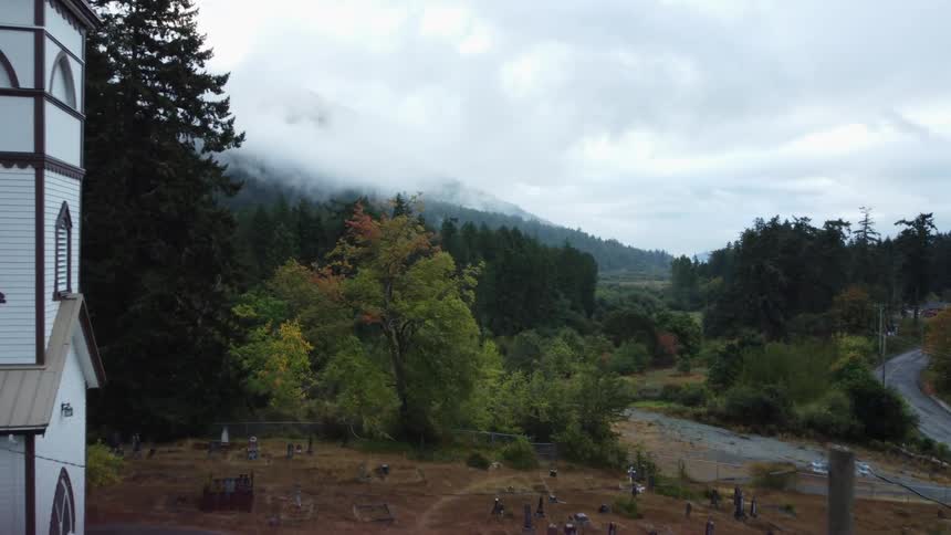 A church with a cemetary in the front lawn sits along a rural highway