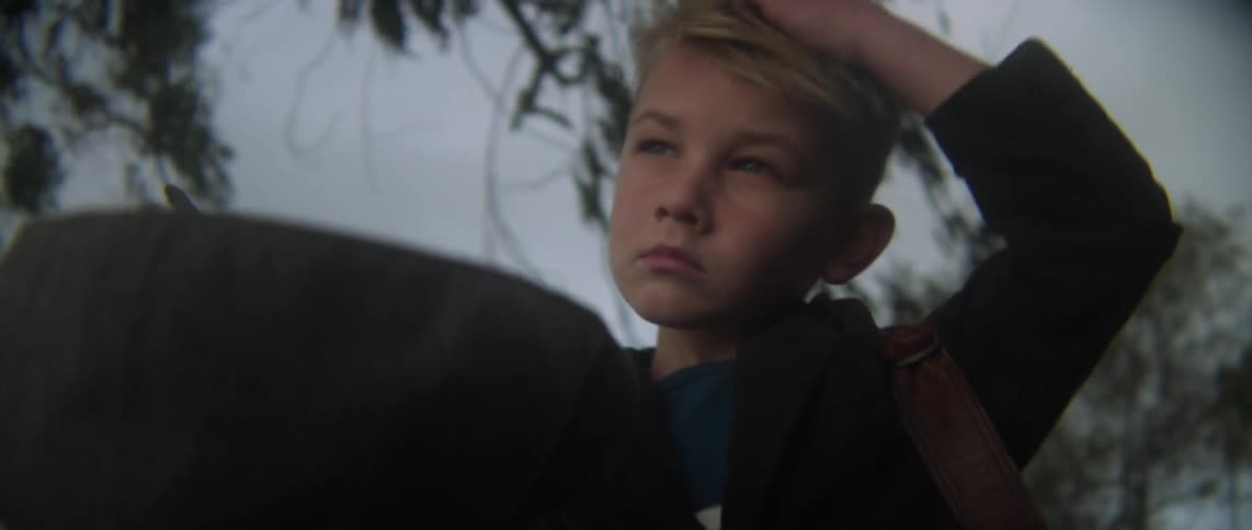 A boy scratches his head and puts his hat on
