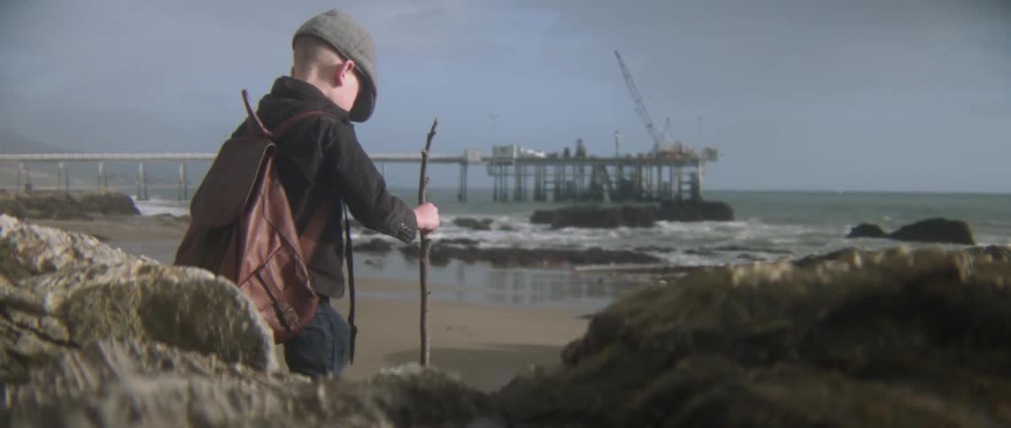 A boy with a stick climbs down a rock