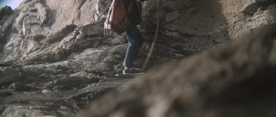 A child walks along rocks with a stick
