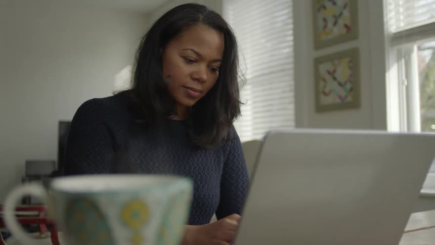 A woman working on a laptop at home with a steaming mug