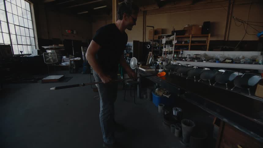 Glass blower takes molten rod from furnace to start shaping it in his studio