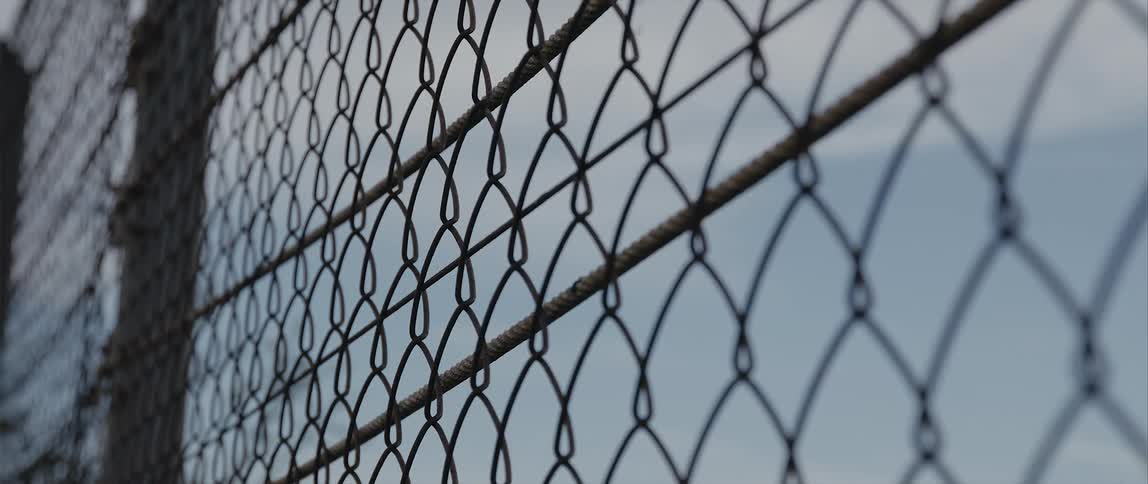 The blue sky shows through a chain link fence