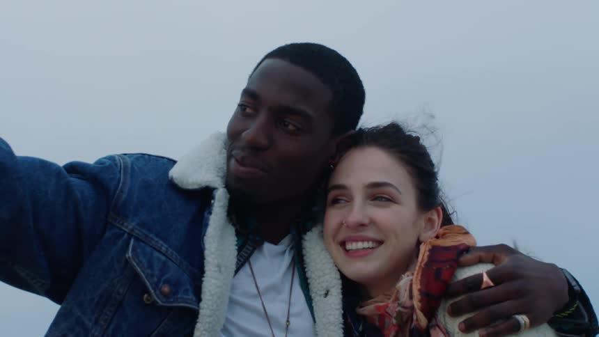 Standing outdoors man hugs woman close as he points then they laugh