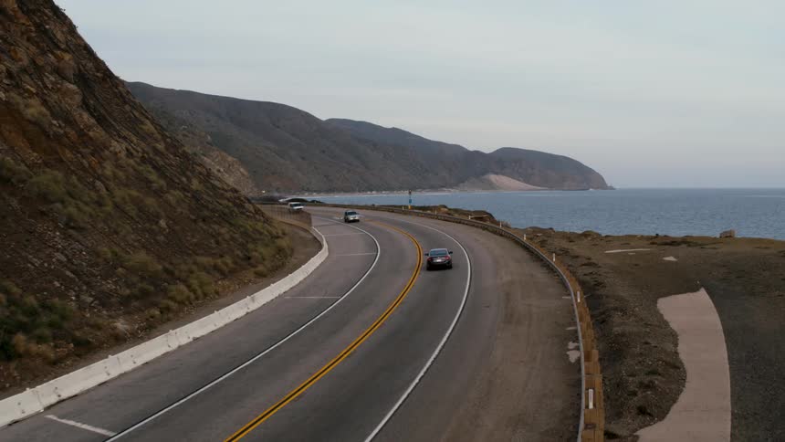 Cars make their way on a winding road through the mountains next to a lake