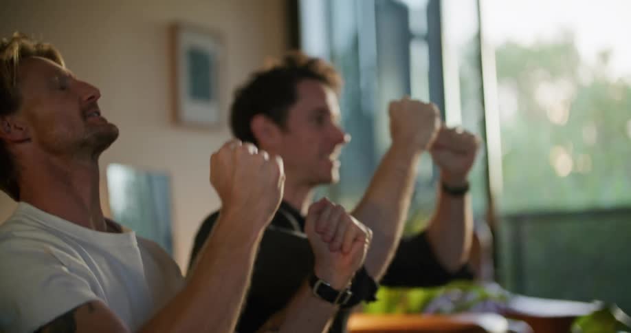 Two men high five while sitting on the couch and watching television