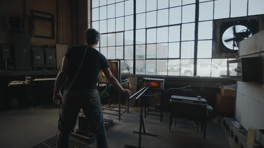 Artist walks over to burning kiln in his industrial studio
