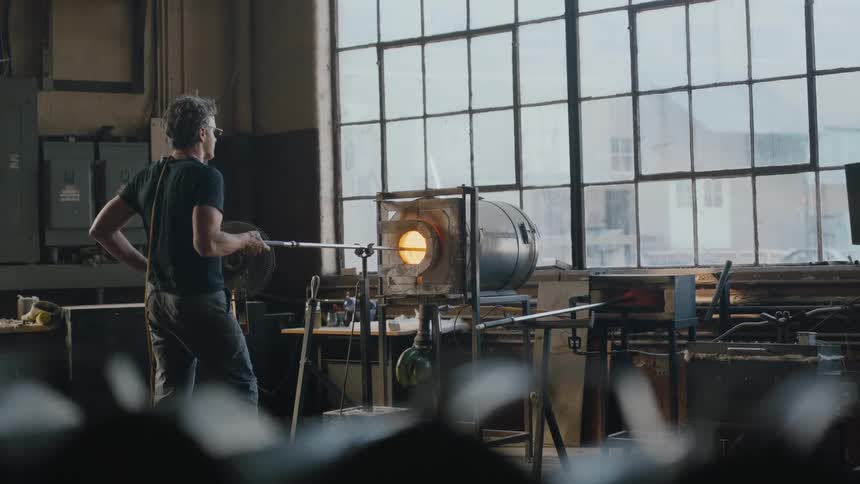 Gritty shot of artist working in his studio blowing glass in electric oven