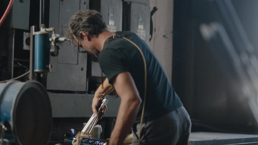 An artisal maker uses tongs to pick up a hot vase he has just created