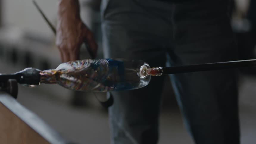 Slow motion of a glass blower carefully turning his work of art to cool it off