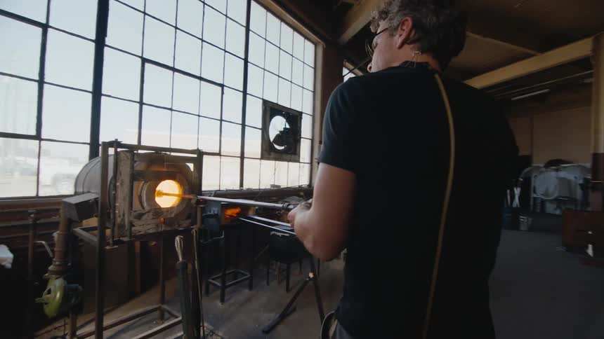 A glass blower turns a rod in a furnace
