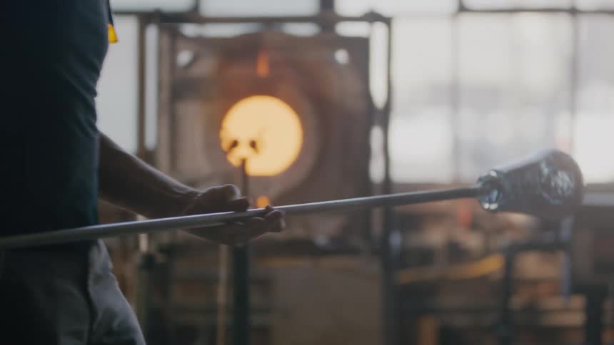 Artist takes molten glass out of furnace and turns it to cool it off