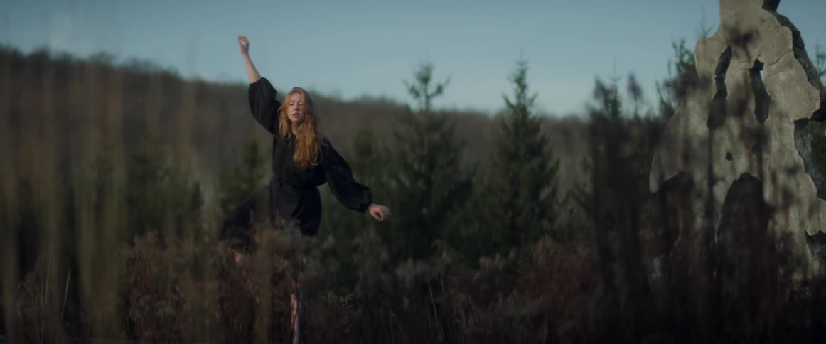 A woman is dancing outdoors in a wooded area