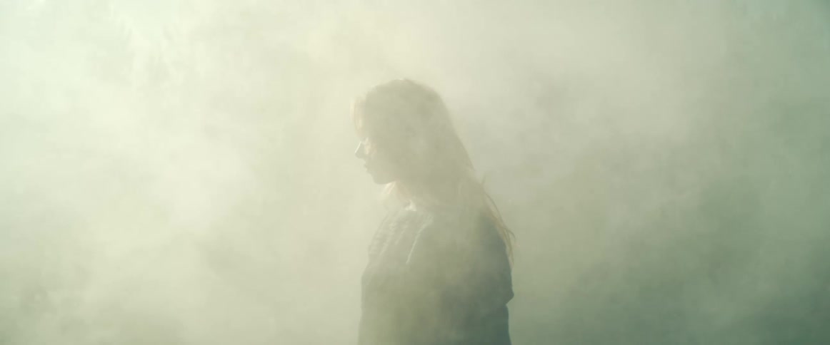 A woman stands surrounded by fog