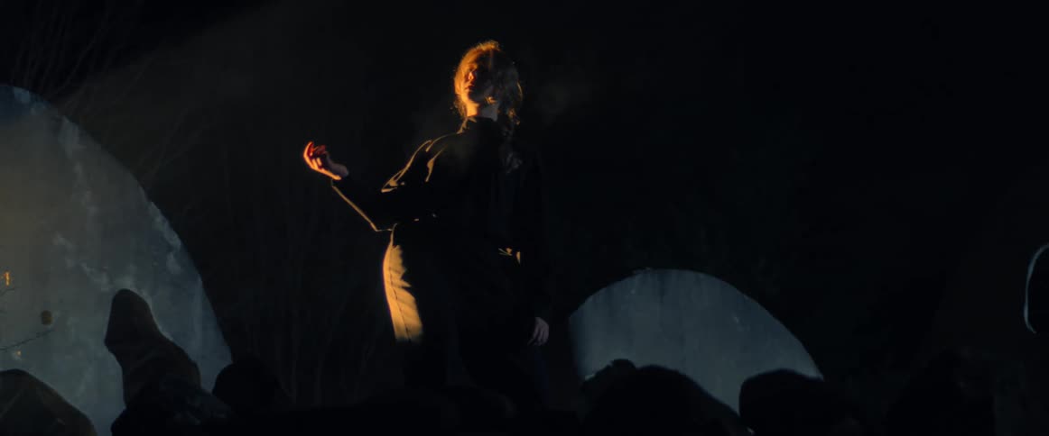 Blonde woman stands on shadowed stage under bright light