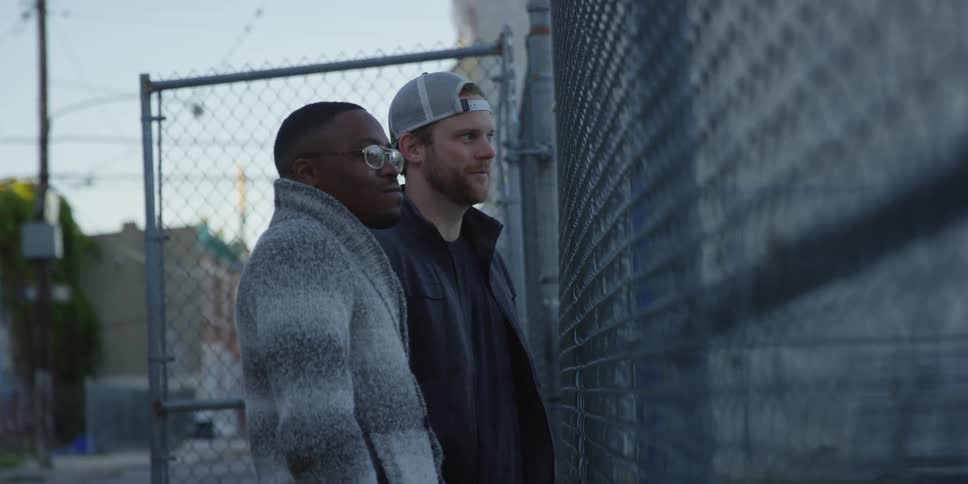 Two men talk near a fence