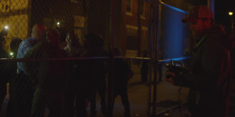 People are filming near a fence with lights flashing at night
