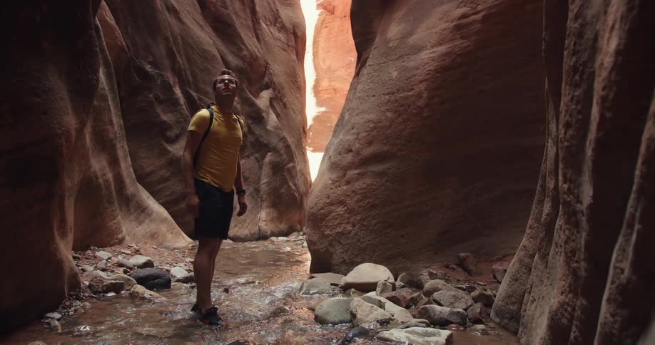 A man carefully steps through a shallow stream at the base of a narrow gorge