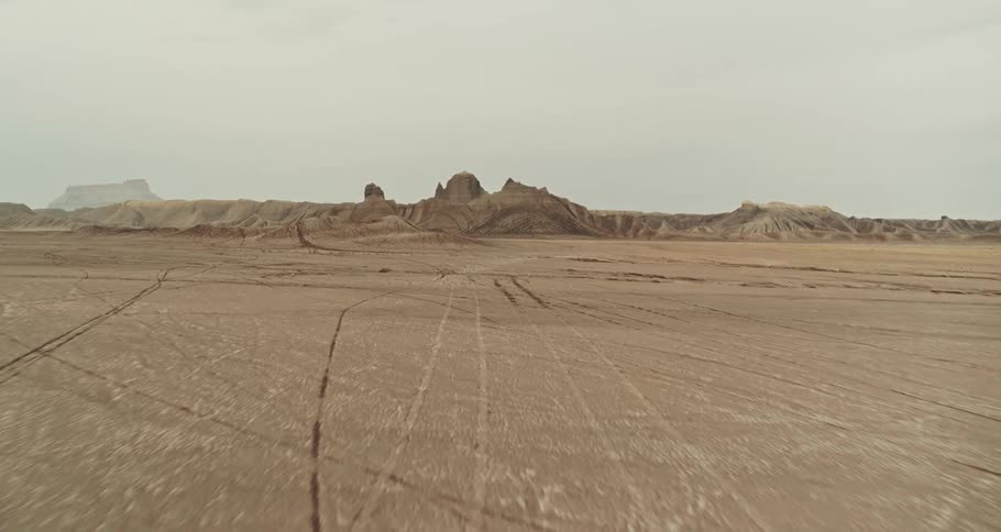 A red truck is traveling across the desert badlands with mountains and buttes in the distance