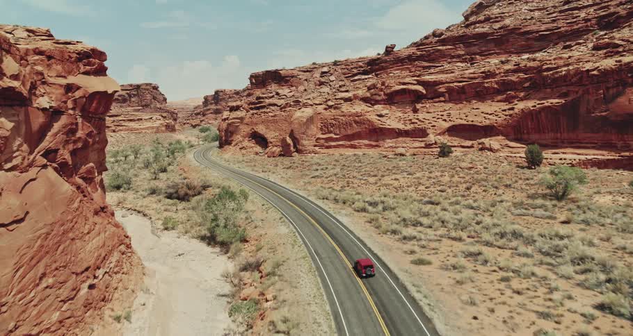 A vehicle travels along a road through arid badlands during the day