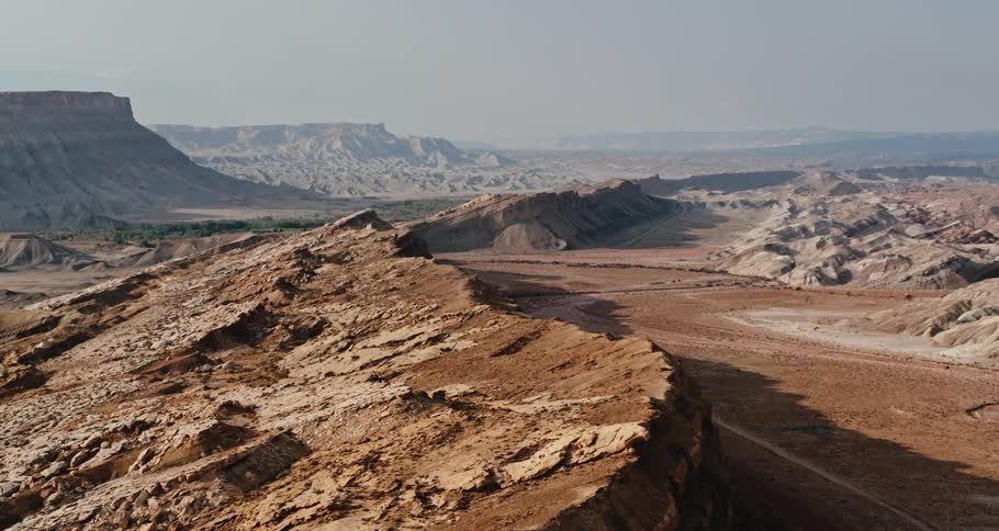 Aerial view of desert badlands as the sun shines on mountains and mesas under a hazy sky