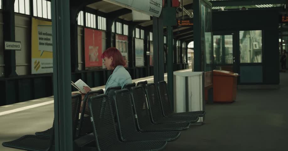 A woman is sitting in a train station reading a book