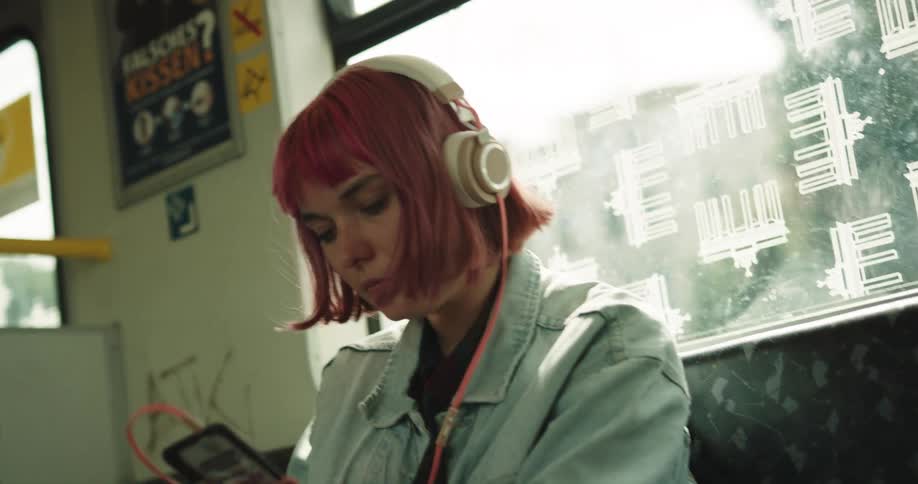 A woman sits on a city bus with headphones looking at her cell phone