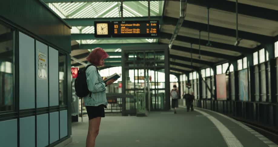 Woman stands in train terminal reading while waiting for the train