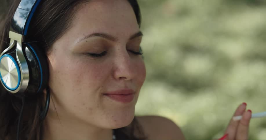 A woman lights a cigarette and smokes it while happily listening to music