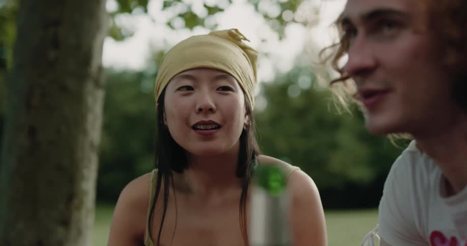 A woman talks with a group of people as they sit and drink together in a field during the day