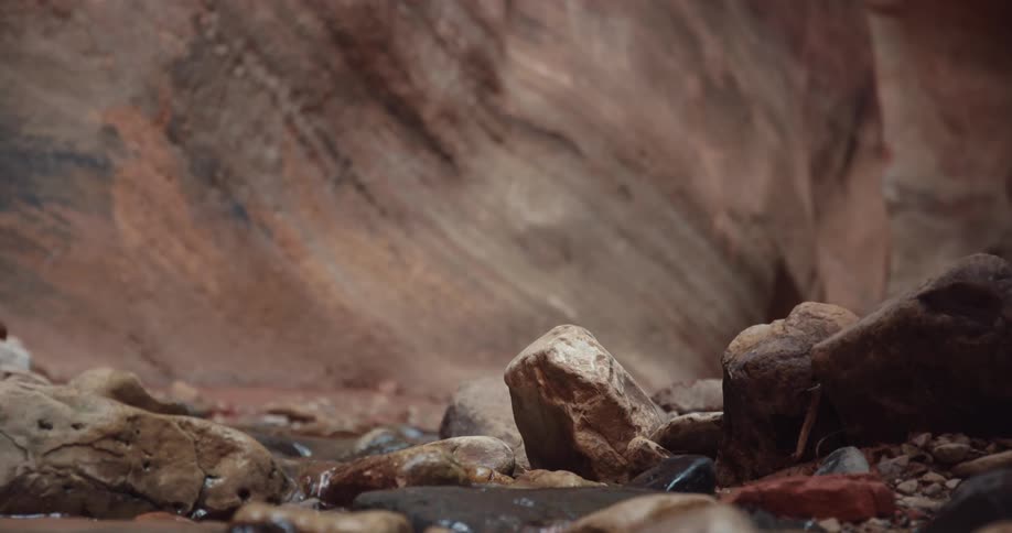 A small stream runs across rocks at the bottom of a ravine during the day