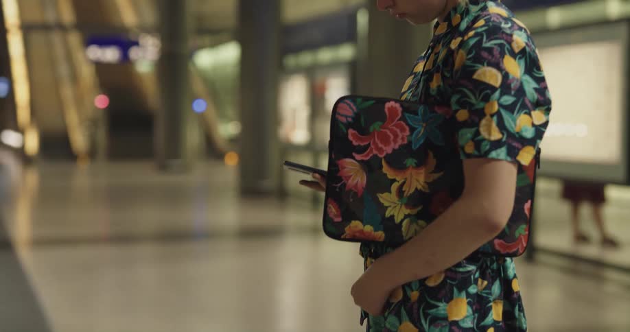 A woman waiting in a train station looks around and checks her phone