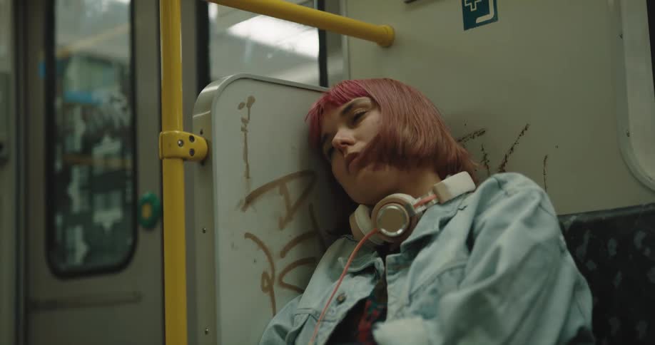 Woman with dyed hair leans sleepily while riding public transportation
