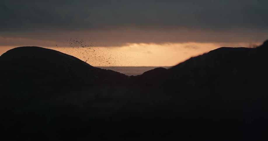 A sunset is seen through shoreline rocks as a sea wave breaks in the air