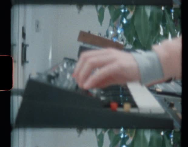Person wearing a pink sweater playing electronic keyboard at home caught on vintage film